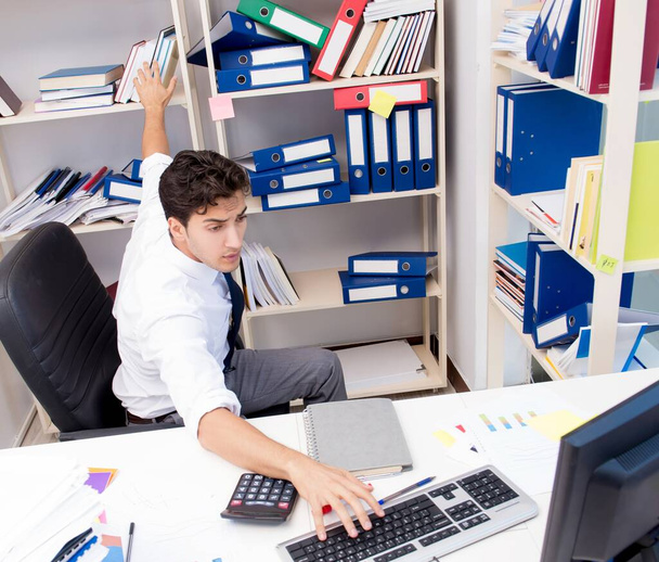 Бизнесмен, работающий в офисе с грудами книг и бумаг - Фото, изображение