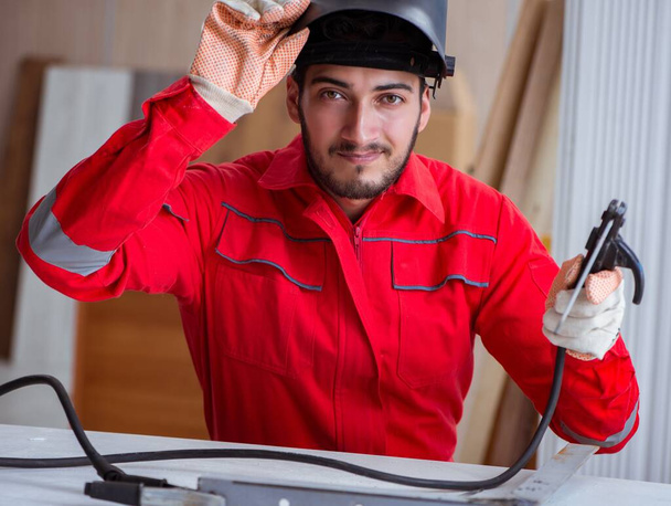 Jonge reparateur met een laspistool elektrode en een helm lassen - Foto, afbeelding