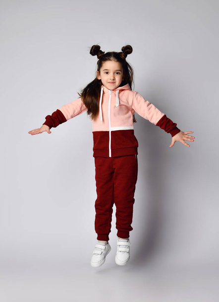 Frolic brunette kid girl in modern fashion pink brown sportwear is jumping having fun - Photo, Image