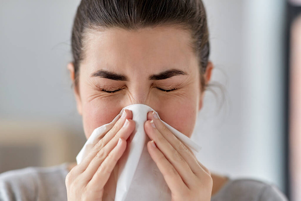 sick woman blowing nose in paper tissue at home - Foto, Imagen