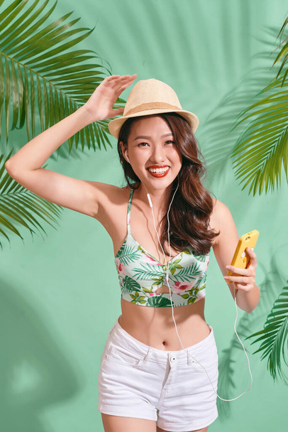 Porträt einer glücklichen Asiatin, die Sommerkleidung trägt und Musik auf blauem Hintergrund hört  - Foto, Bild
