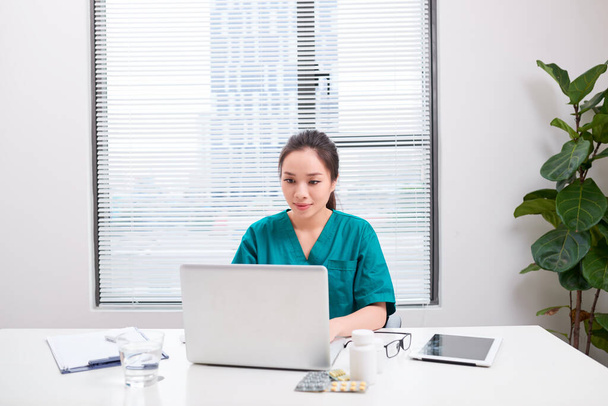 Junge Ärztin bei der Arbeit, während sie im Krankenhausbüro am Laptop tippt. - Foto, Bild