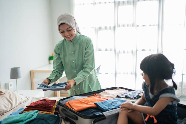 mother prepares clothes and her daughter plays with her suitcase - Photo, image