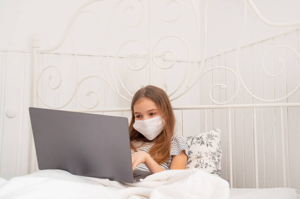a girl in medical mask in bed studying on laptop. - Foto, Imagem