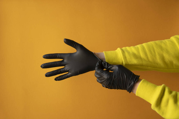 concept, woman puts medical black gloves on her hands, protection 2019-nCoV on yellow background, horizontal frame, copy space, close-up - Photo, Image