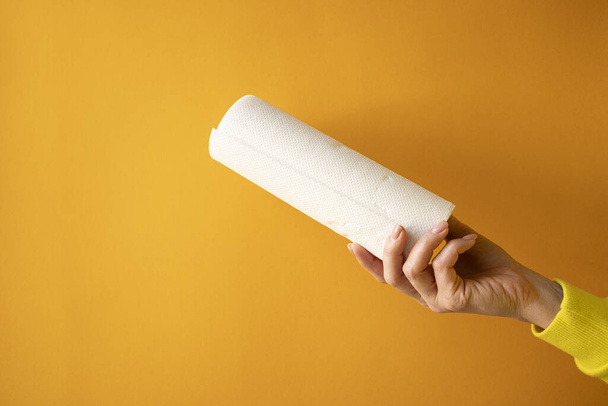 female hand holds a roll of white paper towels on a yellow background, horizontal frame, copy space, close-up - 写真・画像