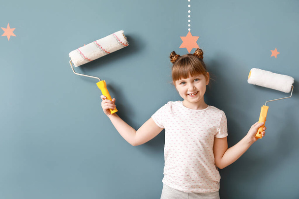 Mała dziewczynka z rolkami farby w pobliżu ściany kolor - Zdjęcie, obraz