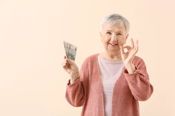 Senior woman with money showing OK on color background - Photo, Image