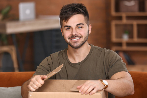 Young man unpacking parcel at home - Foto, afbeelding