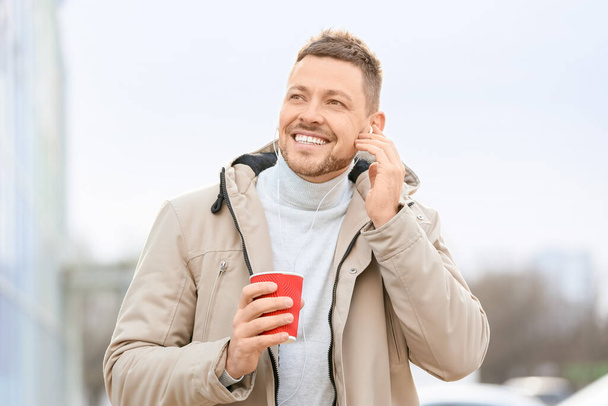 コーヒーを飲みながらハンサムな男は屋外で音楽を聴く - 写真・画像