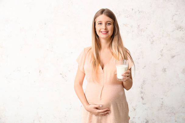 Beautiful pregnant woman with milk on light background - 写真・画像