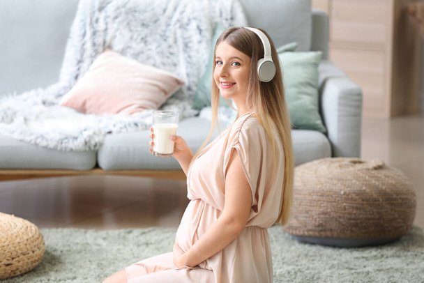 Belle femme enceinte buvant du lait tout en écoutant de la musique à la maison
 - Photo, image