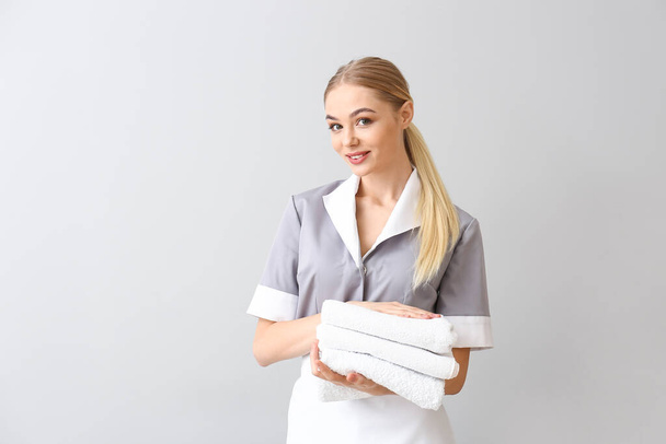 Hermosa joven camarera con toallas sobre fondo claro
 - Foto, Imagen