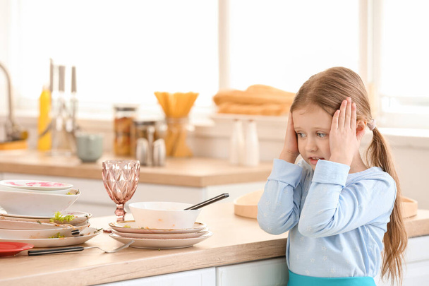 Vonakodó kislány, piszkos edényeket néz a konyhában. - Fotó, kép