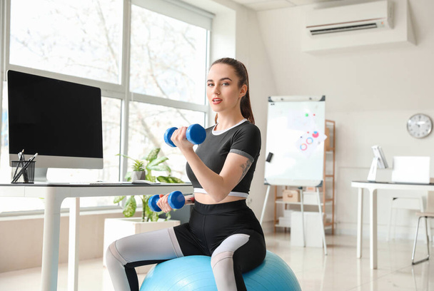 Mujer joven haciendo ejercicios con pelota de fitness en la oficina
 - Foto, imagen