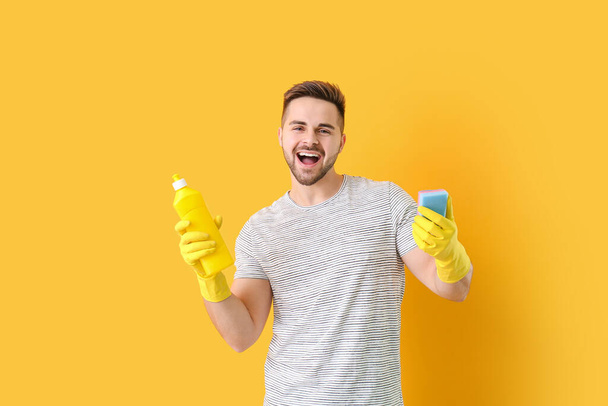 Ευτυχισμένος άνθρωπος με απορρυπαντικό και σφουγγάρι στο φόντο χρώμα - Φωτογραφία, εικόνα