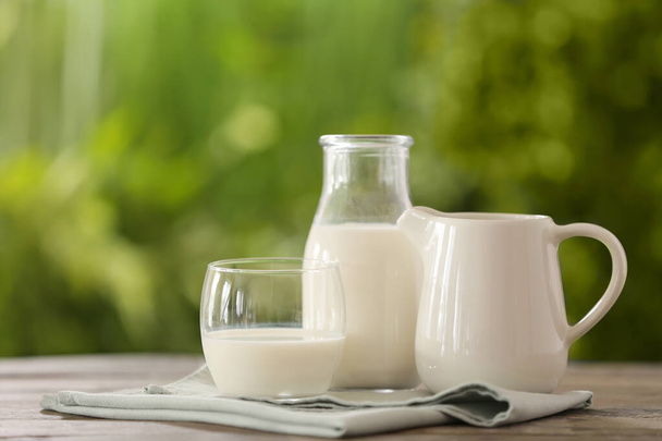 Copo, jarro e garrafa de leite fresco na mesa ao ar livre
 - Foto, Imagem