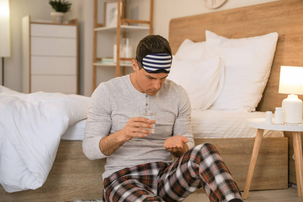 Young man taking pills for insomnia in bedroom - Photo, image
