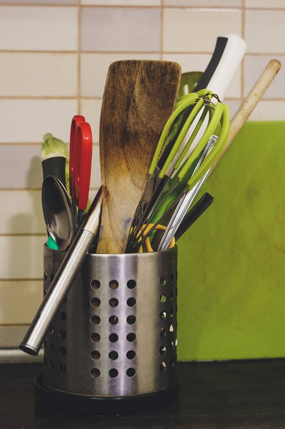 A mix of kitchen cooking utensils in a metal holder on a kitchen counter - Fotó, kép