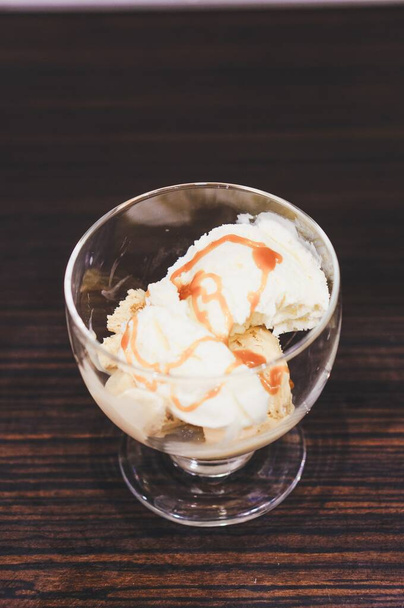 A top view of ice cream topped with caramel syrup in a glass cup on a wooden table - Foto, afbeelding