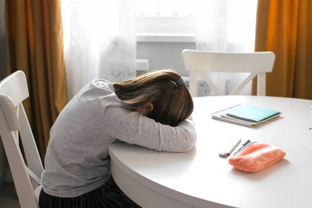 Χαριτωμένη μαθήτρια, 7-8 ετών, κοιμάται στο τραπέζι. Σπίτι σχολείο, online εκπαίδευση, κατ 'οίκον εκπαίδευση, καραντίνα, έννοια coronavirus - Φωτογραφία, εικόνα