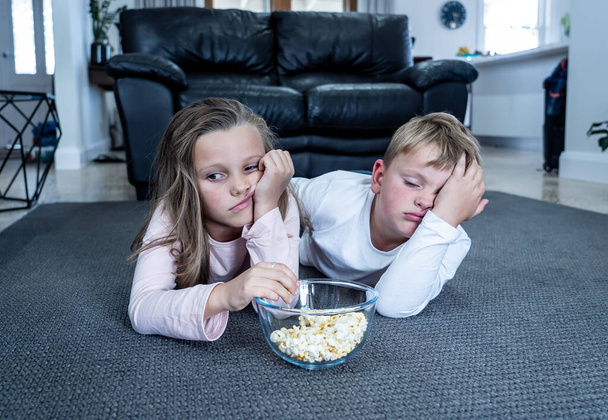 Coronavirus lockdow. Bored little girl and sad boy watching tv in isolation at home during quarantine COVID 19 Outbreak. Mandatory lockdowns and school closures impact on children mental health. - Foto, Imagen