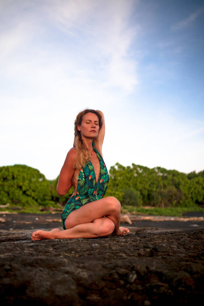 Outdoor yoga praktijk. Jonge vrouw die Gomukhasana beoefent, Cow Face Pose, zittend asana in hatha yoga. Een vrouw die haar handen op haar rug houdt en zich uitstrekt. Zelfzorgconcept. Strand van Tanah Lot, Bali - Foto, afbeelding