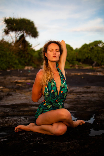 Outdoor yoga praktijk. Jonge vrouw die Gomukhasana beoefent, Cow Face Pose, zittend asana in hatha yoga. Een vrouw die haar handen op haar rug houdt en zich uitstrekt. Zelfzorgconcept. Strand van Tanah Lot, Bali - Foto, afbeelding
