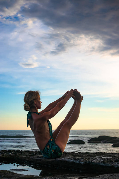 Outdoor yoga practice. Attractive woman practicing Ubhaya Padangusthasana, Wide-Angle Seated Forward Bend. Strengthen legs and core. Self care concept. Yoga retreat. Tanah Lot beach, Bali. - Photo, Image