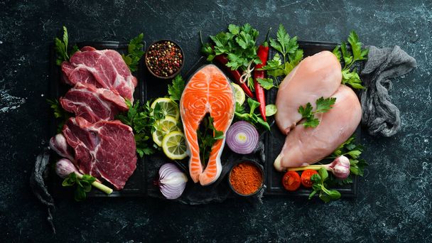 Set of meat. Fish steak, veal steak and chicken breast. Top view. On a black stone background. - Foto, Imagen