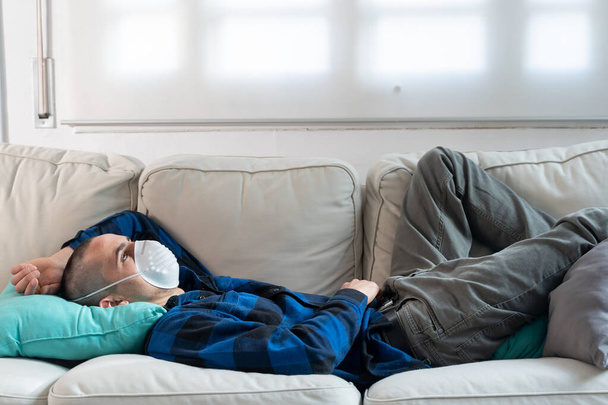Coronavirus. Man at home wearing protective mask. Woman in quarantine for coronavirus on the couch cleaning her hands with sanitizer gel. Working from home. Clean your hands with sanitizer gel.  - Foto, Bild