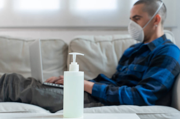 Coronavirus. Man at home wearing protective mask. Woman in quarantine for coronavirus on the couch cleaning her hands with sanitizer gel. Working from home. Clean your hands with sanitizer gel.  - Valokuva, kuva