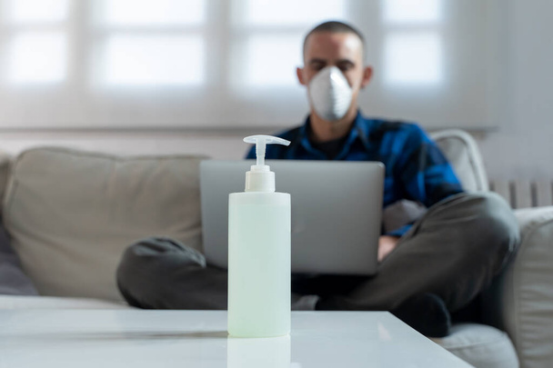 Coronavirus. Man at home wearing protective mask. Woman in quarantine for coronavirus on the couch cleaning her hands with sanitizer gel. Working from home. Clean your hands with sanitizer gel.  - Photo, Image