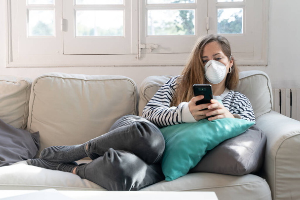 Coronavirus. Woman at home wearing protective mask. Woman in quarantine for coronavirus on the couch cleaning her hands with sanitizer gel. Working from home. Clean your hands with sanitizer gel.  - Фото, зображення