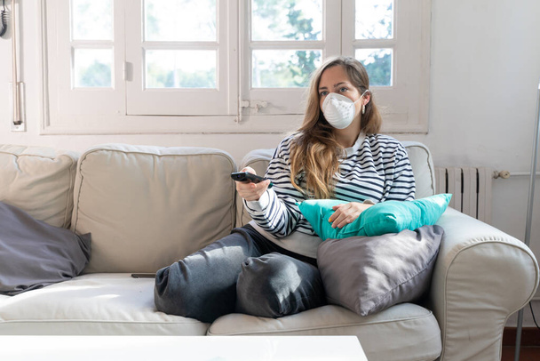Coronavirus. Woman at home wearing protective mask. Woman in quarantine for coronavirus on the couch cleaning her hands with sanitizer gel. Working from home. Clean your hands with sanitizer gel.  - Foto, Imagen