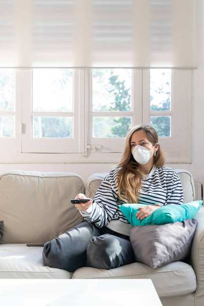 Coronavirus. Woman at home wearing protective mask. Woman in quarantine for coronavirus on the couch cleaning her hands with sanitizer gel. Working from home. Clean your hands with sanitizer gel.  - Foto, Imagem
