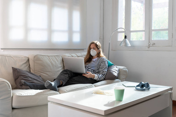 Coronavirus. Woman at home wearing protective mask. Woman in quarantine for coronavirus on the couch cleaning her hands with sanitizer gel. Working from home. Clean your hands with sanitizer gel.  - Photo, Image