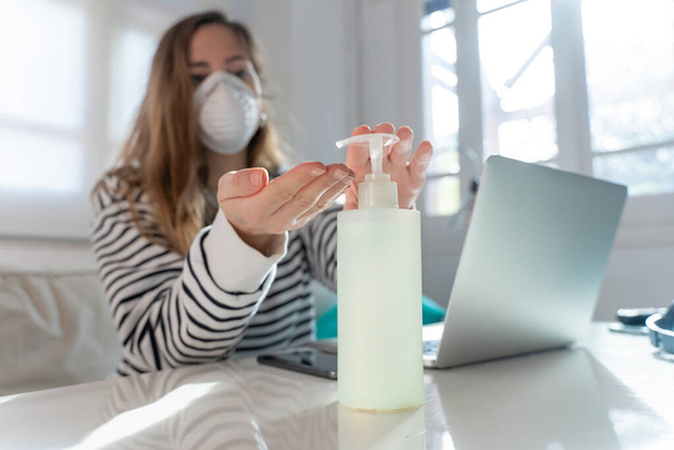 Coronavirus. Woman at home wearing protective mask. Woman in quarantine for coronavirus on the couch cleaning her hands with sanitizer gel. Working from home. Clean your hands with sanitizer gel.  - Foto, imagen