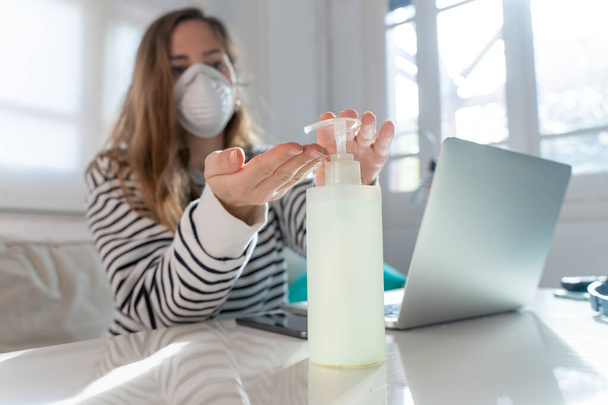 Coronavirus. Woman at home wearing protective mask. Woman in quarantine for coronavirus on the couch cleaning her hands with sanitizer gel. Working from home. Clean your hands with sanitizer gel.  - Foto, Bild
