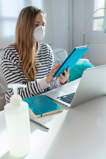 Coronavirus. Woman at home wearing protective mask. Woman in quarantine for coronavirus on the couch cleaning her hands with sanitizer gel. Working from home. Clean your hands with sanitizer gel.  - Foto, Imagem