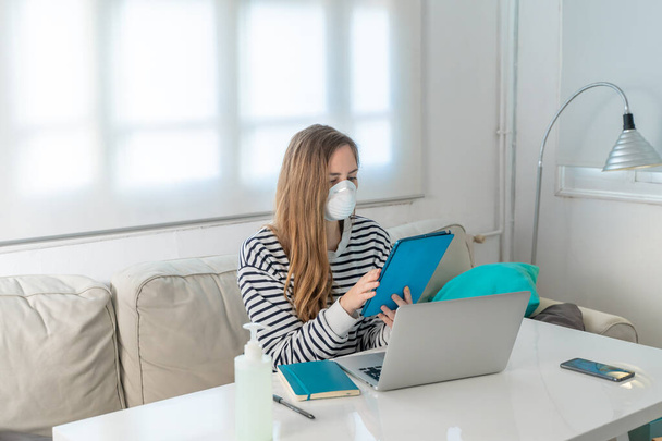 Coronavirus. Woman at home wearing protective mask. Woman in quarantine for coronavirus on the couch cleaning her hands with sanitizer gel. Working from home. Clean your hands with sanitizer gel.  - Fotoğraf, Görsel