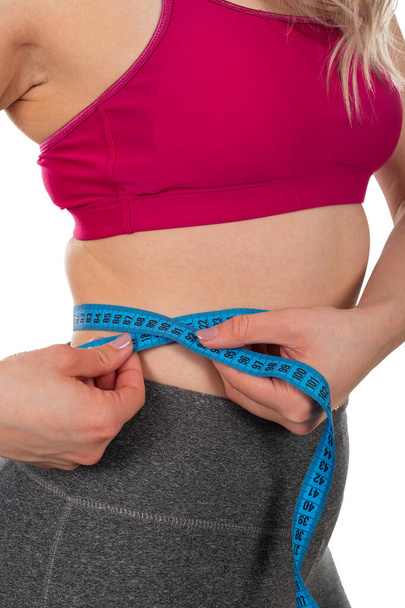 Cintura de las hembras jóvenes, sosteniendo una cinta métrica sobre un fondo aislado: pérdida de peso, dieta, concepto de conformación corporal
 - Foto, imagen