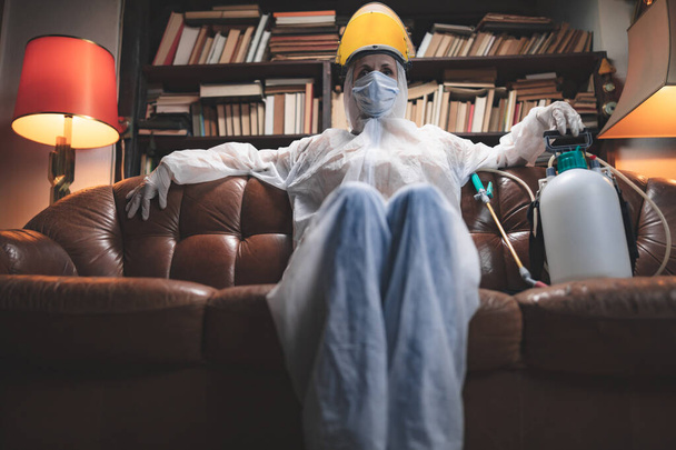 Persona con máscara antiviral protectora, botella de pulverizador de descontaminación química en aislamiento casero
. - Foto, imagen