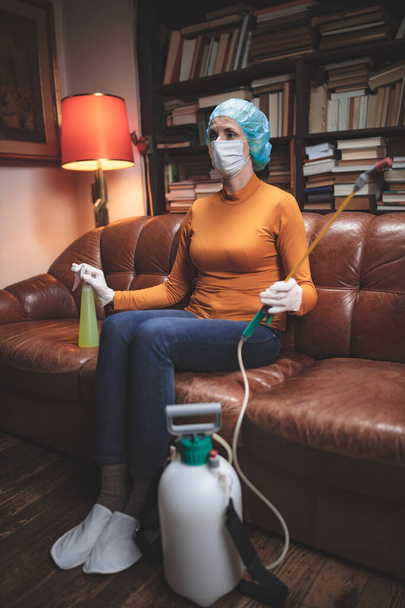 Kobieta z ochronną maską przeciwwirusową, chemicznym rozpylaczem w izolacji domowej. - Zdjęcie, obraz