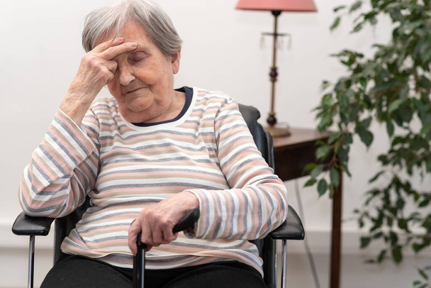 Пожилая женщина сидит и у нее болит голова
 - Фото, изображение