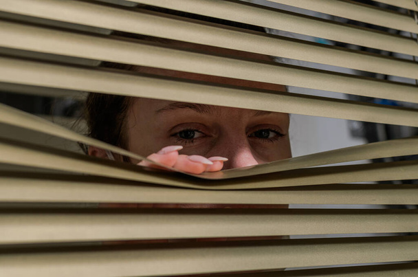 Young woman looking out the window through the blinds - Foto, imagen