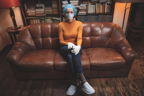 Mulher com máscara antiviral protetora sentada em casa em isolamento / quarentena
. - Foto, Imagem