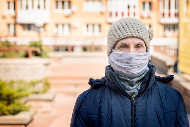 Zavallı yaşlı bir kadın, kendini koronavirüs, covid-19 ya da SARS ve MERS gibi virüslerden korumak için ev yapımı bir maske takıyor. Şehir ortamında yaşıyor. - Fotoğraf, Görsel