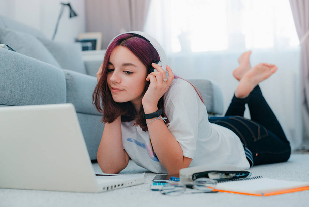 Genç kız liseli kız kulaklıklar takıyor oturma odası öğrencisi laptopuyla ev ödevi yapıyor. Covid-19 Coronavirüs karantinası sırasında uzaktan öğrenme eğitimini kavramsal olarak kabul et - Fotoğraf, Görsel