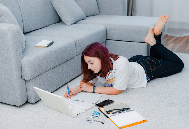 młoda dziewczyna nastoletnia uczennica leżąca piętro salon sofa student studiuje w domu pracując z laptopem odrabiając lekcje. Koncepcja kształcenia na odległość podczas kwarantanny koronawirusu covid-19 - Zdjęcie, obraz